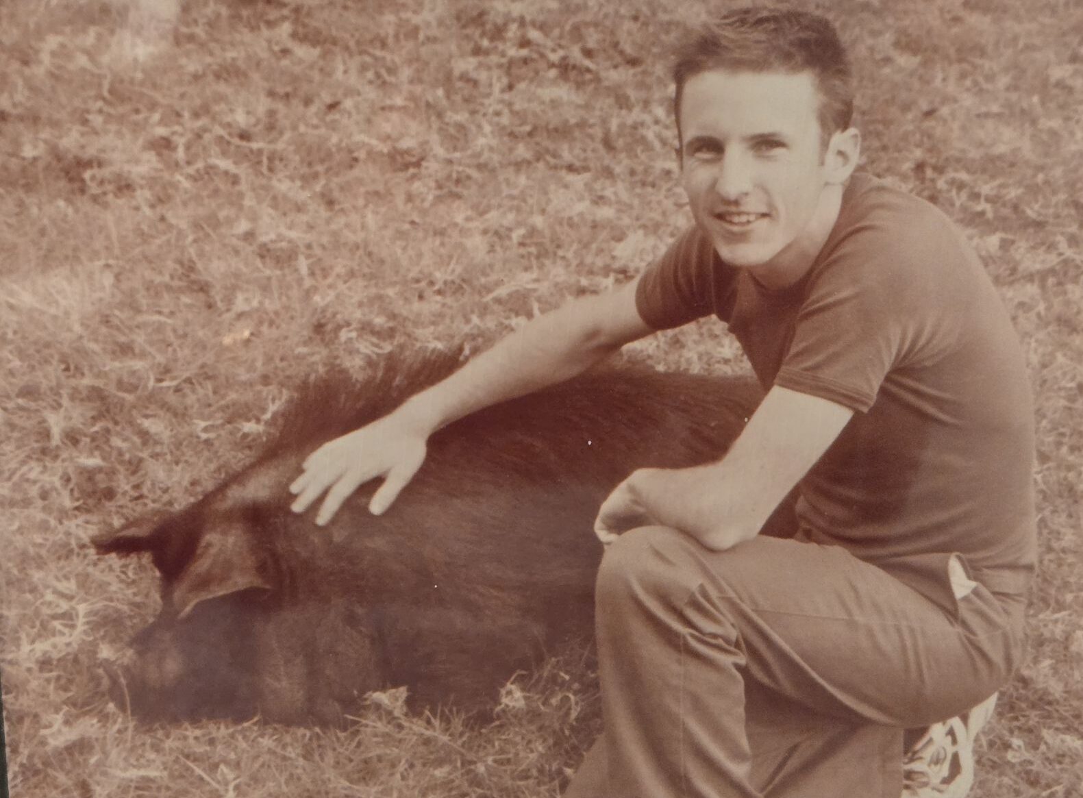 a man sitting on grass with a kunekune pig